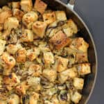 A rustic cast iron skillet filled with wild mushroom and herb sourdough stuffing, topped with crispy edges and a drizzle of garlic olive oil.