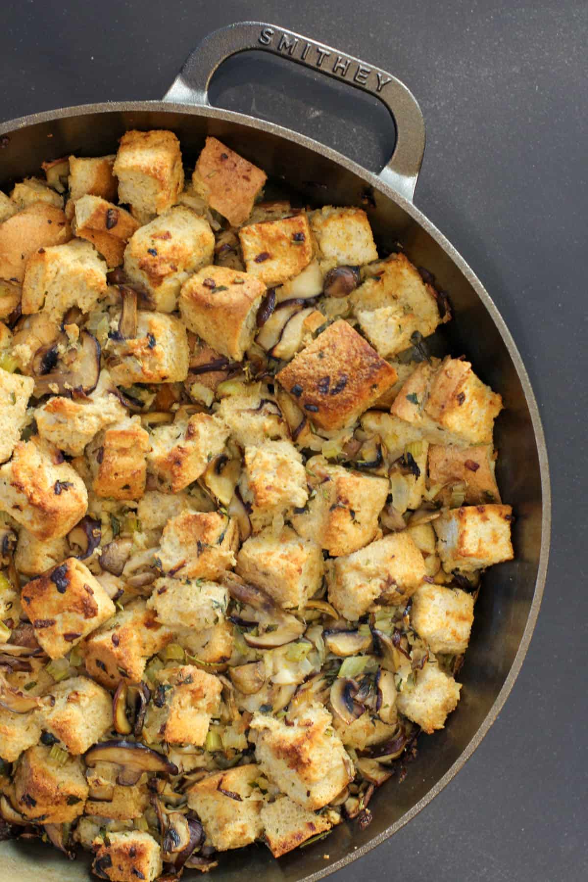 A rustic cast iron skillet filled with wild mushroom and herb sourdough stuffing, topped with crispy edges and a drizzle of garlic olive oil.