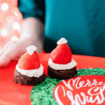 Mini Santa brownie bites topped with fresh strawberries and whipped cream arranged on a holiday platter. A festive bite-sized Christmas dessert for parties and entertaining.