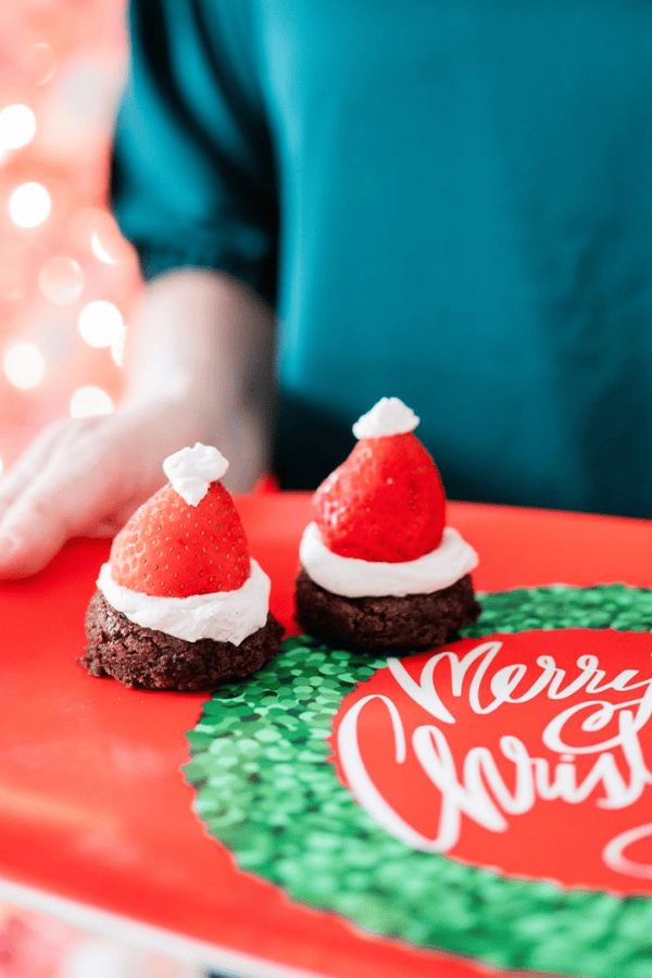 Mini Santa brownie bites topped with fresh strawberries and whipped cream arranged on a holiday platter. A festive bite-sized Christmas dessert for parties and entertaining.