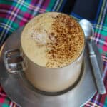 Homemade gingerbread latte with frothy milk and cinnamon on top, served in a glass mug on a plaid holiday table