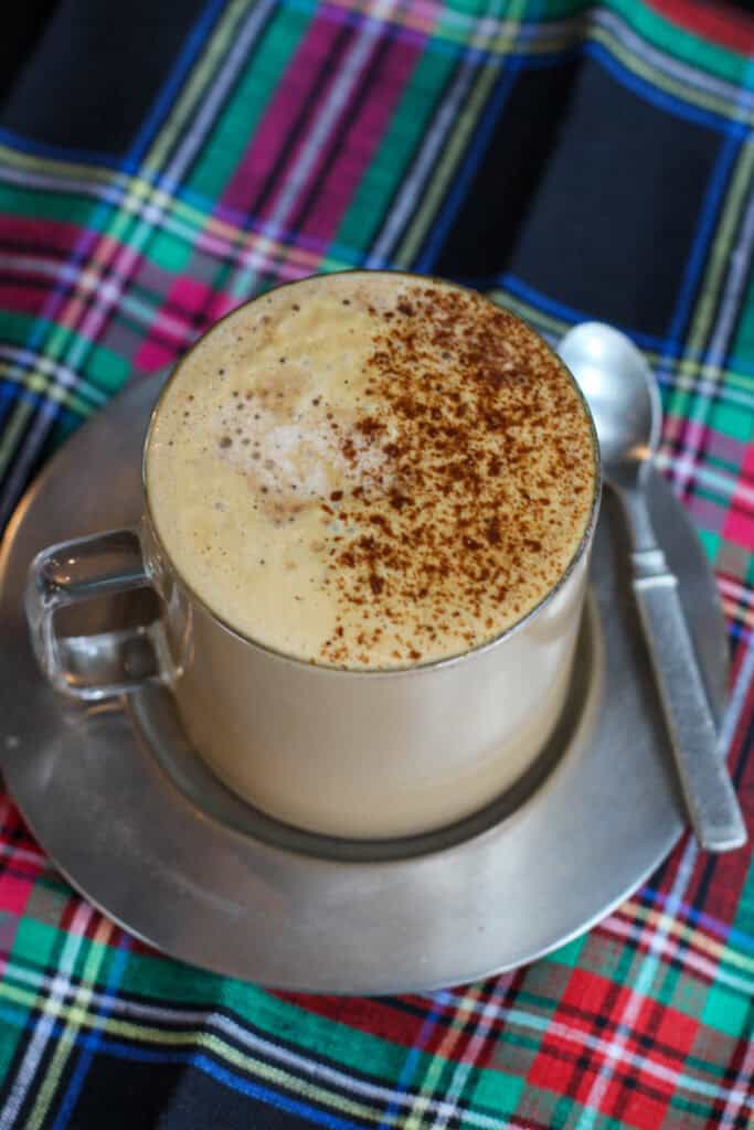 Homemade gingerbread latte with frothy milk and cinnamon on top, served in a glass mug on a plaid holiday table