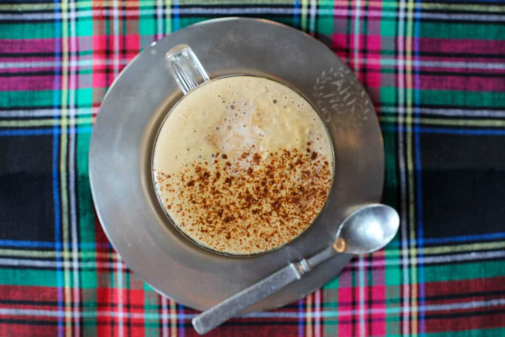 Homemade gingerbread latte with frothy milk and cinnamon on top, served in a glass mug on a plaid holiday table
