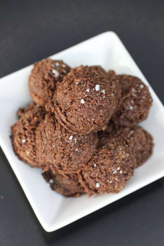 Chocolate sea salt protein bites stacked in a white serving bowl, made with almond flour and chocolate protein powder, finished with a light sprinkle of flaky sea salt on a dark background.