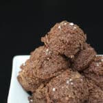 Chocolate sea salt protein bites stacked in a white serving bowl, made with almond flour and chocolate protein powder, finished with a light sprinkle of flaky sea salt on a dark background.