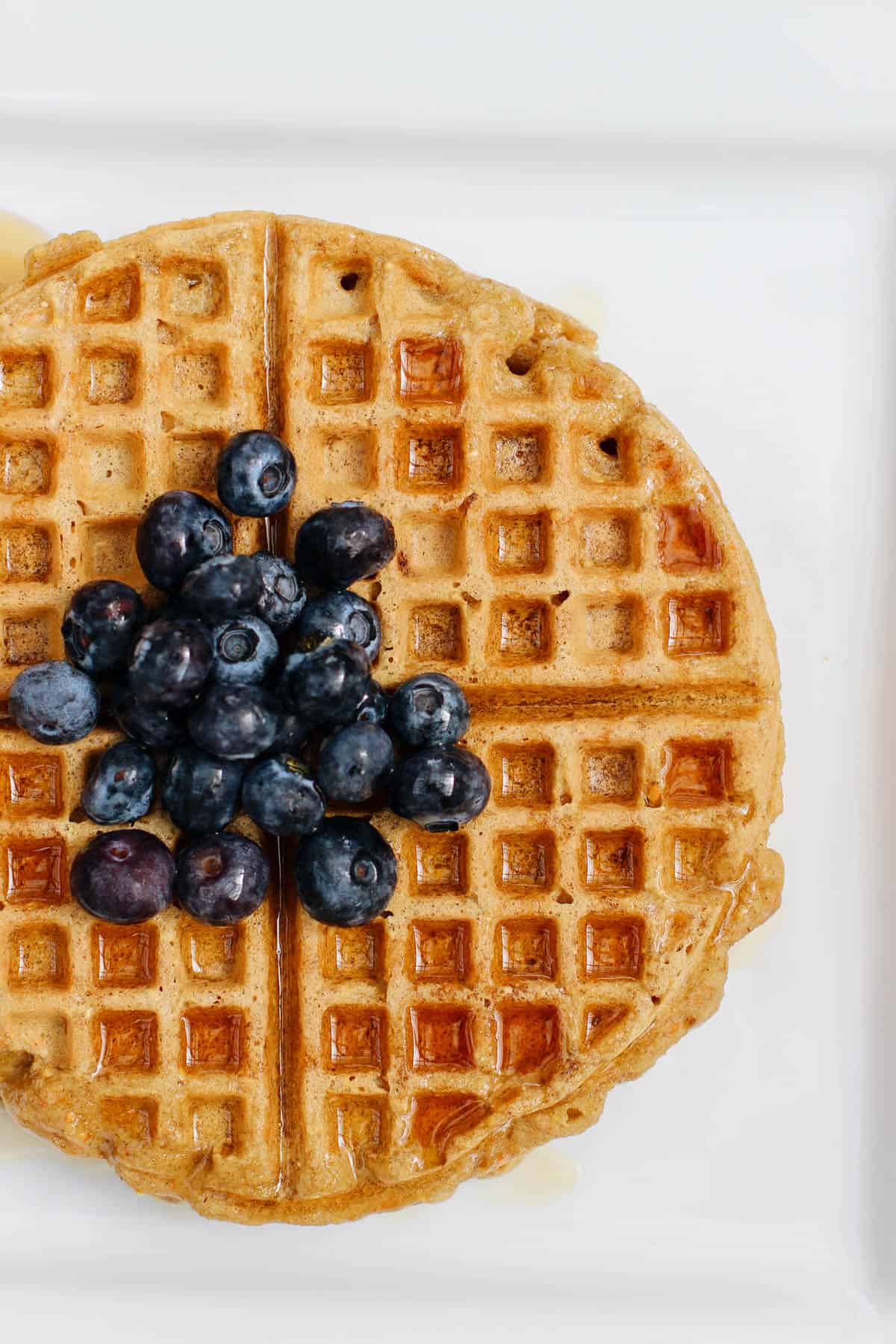 Gluten-free buttermilk waffles topped with fresh blueberries and maple syrup on a white plate