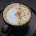 Maple cinnamon latte topped with creamy foam and a light dusting of cinnamon in a black ceramic mug