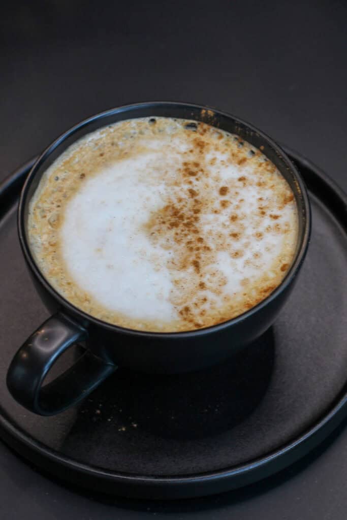 Maple cinnamon latte topped with creamy foam and a light dusting of cinnamon in a black ceramic mug