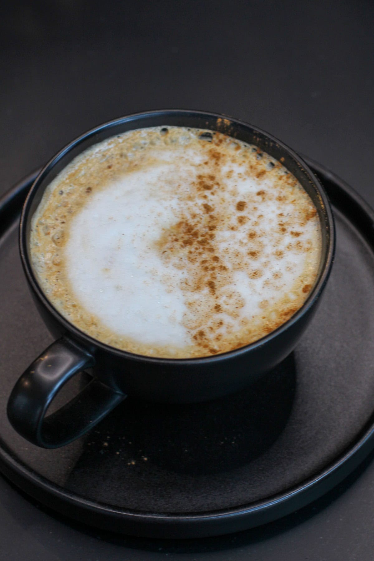 Maple cinnamon latte topped with creamy foam and a light dusting of cinnamon in a black ceramic mug