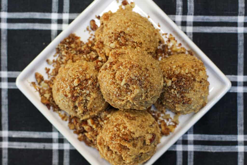No-bake maple pecan protein bites made with almond flour, chopped pecans, maple syrup, and cinnamon, arranged on a white serving dish.