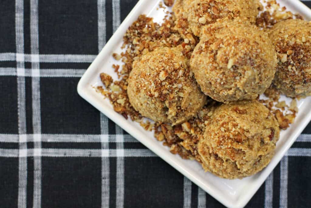 No-bake maple pecan protein bites made with almond flour, chopped pecans, maple syrup, and cinnamon, arranged on a white serving dish.