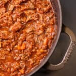 Slow-braised beef ragú simmering in a cast iron Dutch oven, with tender shredded beef in a rich tomato and red wine sauce.