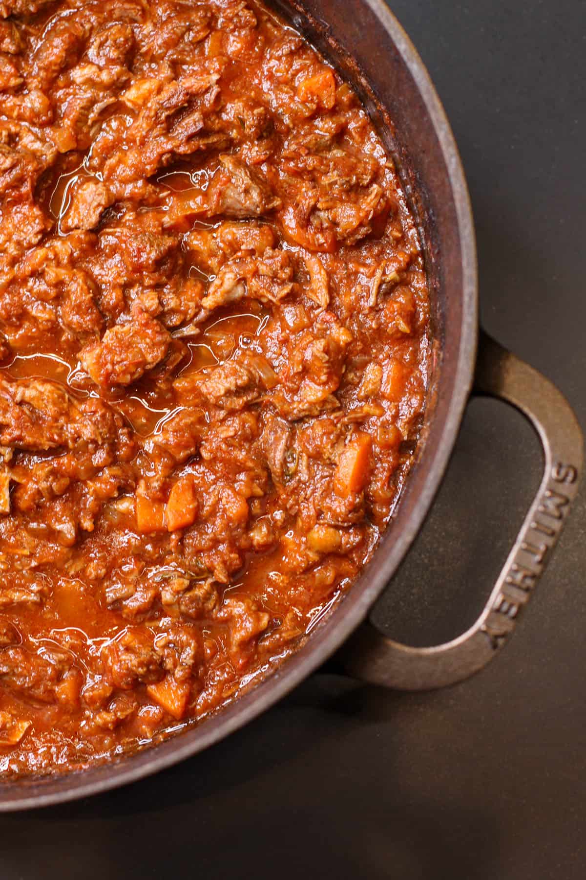 Slow-braised beef ragú simmering in a cast iron Dutch oven, with tender shredded beef in a rich tomato and red wine sauce.
