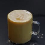 Glass mug of maple sweetened vanilla cardamom latte topped with foam on a dark background