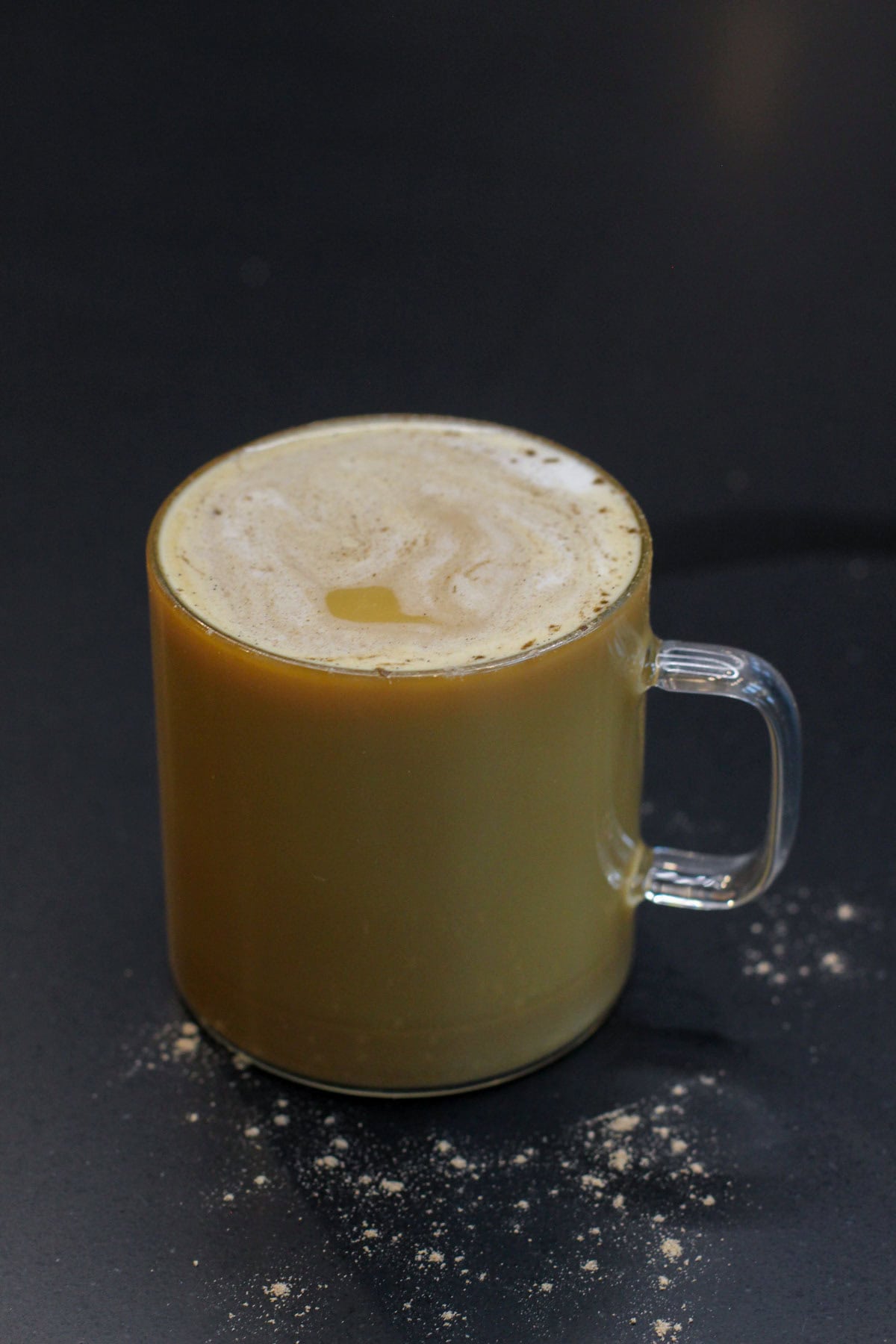 Glass mug of maple sweetened vanilla cardamom latte topped with foam on a dark background