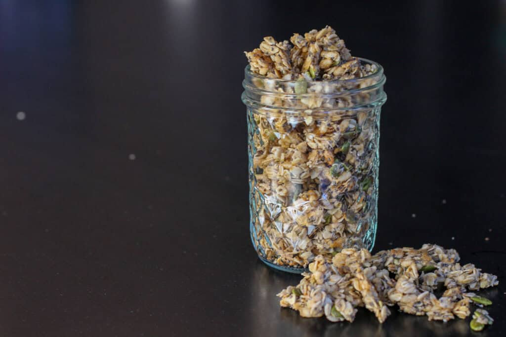 Crunchy ancient grain granola with oats, chia seeds, pumpkin seeds, and shredded coconut in a glass jar