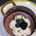 Silky dark chocolate pots de crème topped with whipped cream, fresh berries, and mint in a small copper pan for an elegant dinner party dessert.