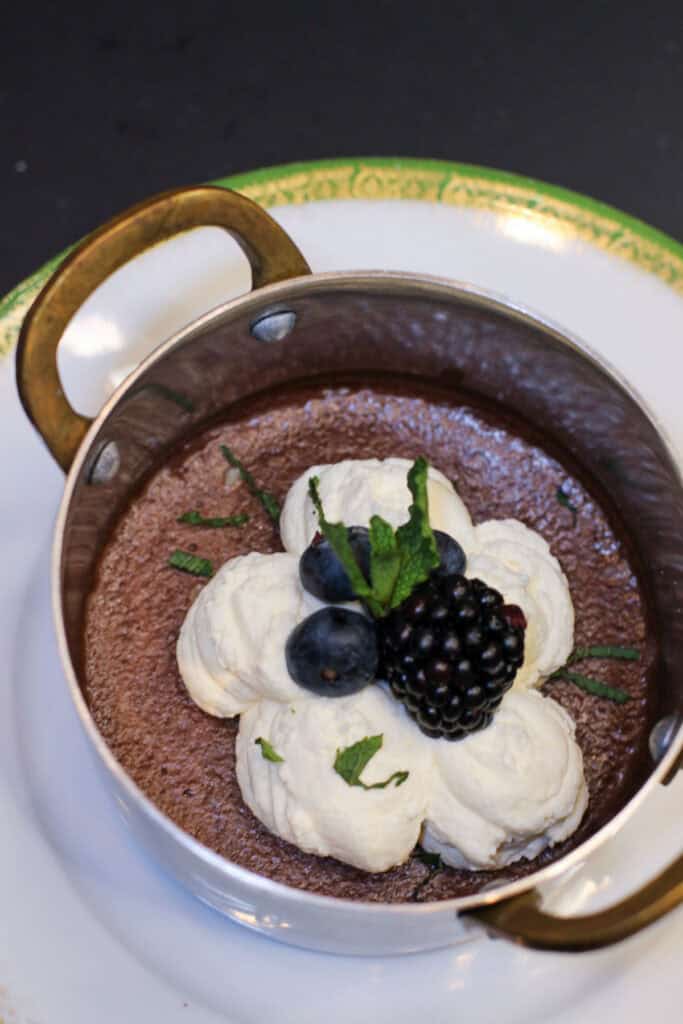 Silky dark chocolate pots de crème topped with whipped cream, fresh berries, and mint in a small copper pan for an elegant dinner party dessert.