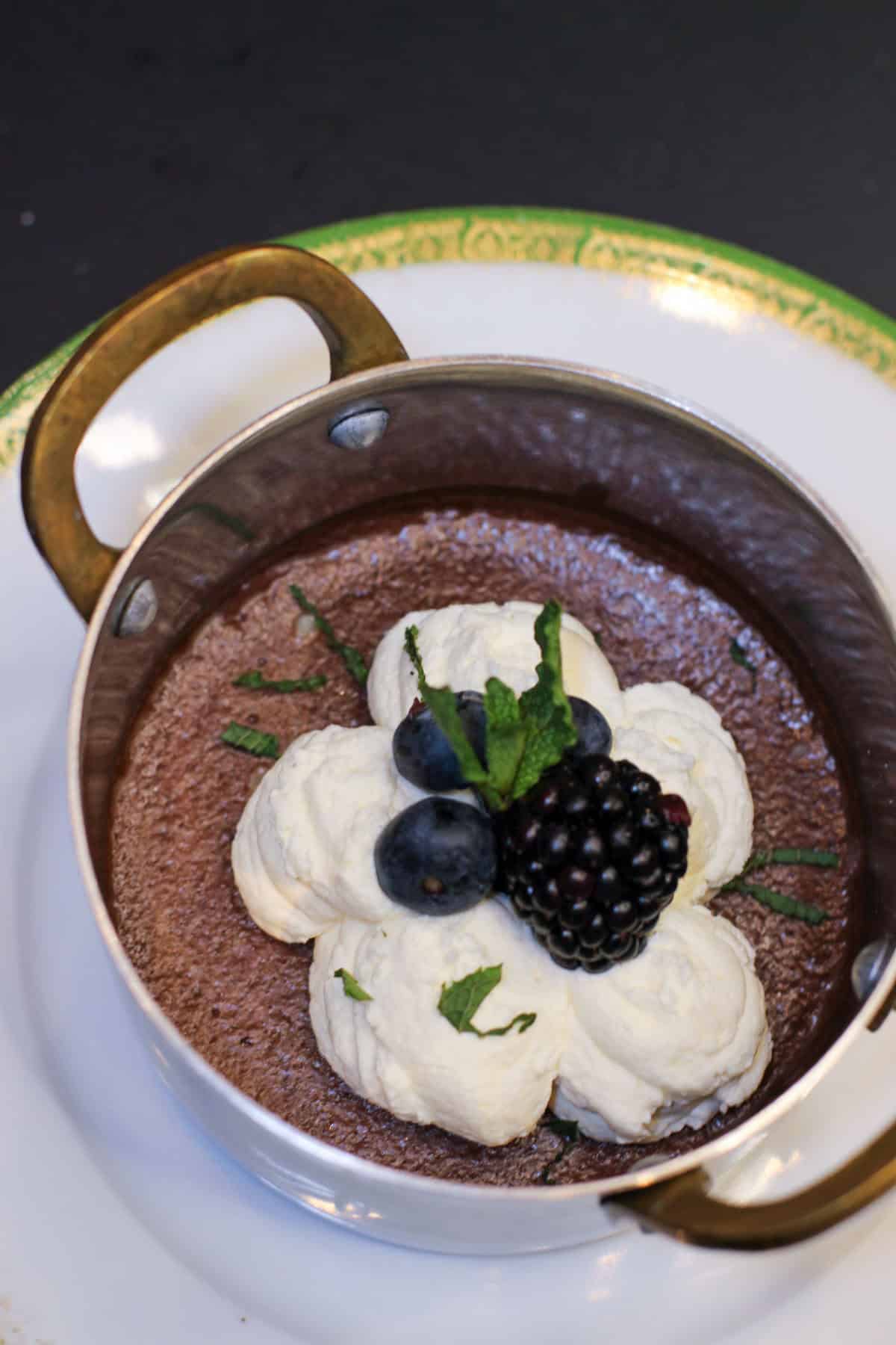 Silky dark chocolate pots de crème topped with whipped cream, fresh berries, and mint in a small copper pan for an elegant dinner party dessert.