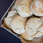 Golden gluten-free biscuits stacked in a metal baking pan lined with parchment paper, showing flaky edges and a soft, rustic texture.