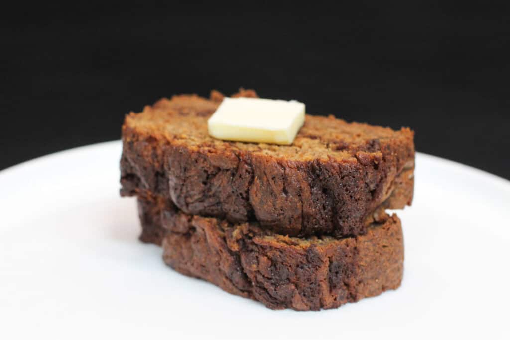 Brown butter cinnamon swirl banana bread slices stacked on a white plate, topped with melting butter, showing a moist crumb and rich, caramelized edges