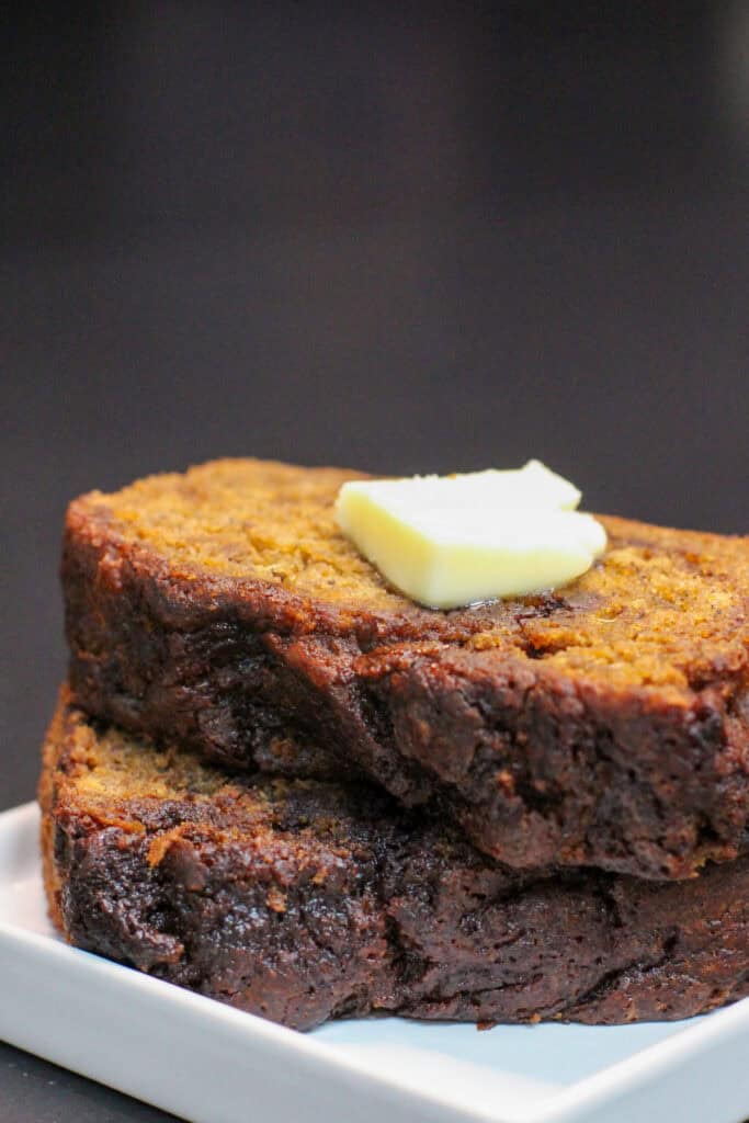 Brown butter cinnamon swirl banana bread slices stacked on a white plate, topped with melting butter, showing a moist crumb and rich, caramelized edges
