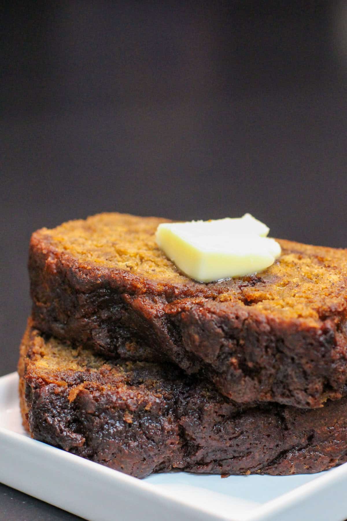 Brown butter cinnamon swirl banana bread slices stacked on a white plate, topped with melting butter, showing a moist crumb and rich, caramelized edges