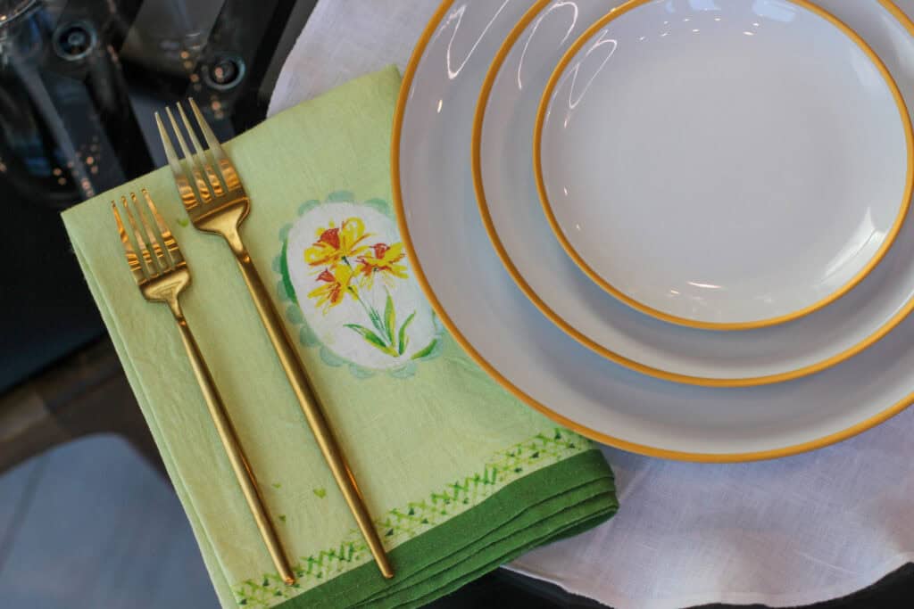 Simple spring table setting with green floral linen napkin, gold flatware, and layered white plates with gold rim