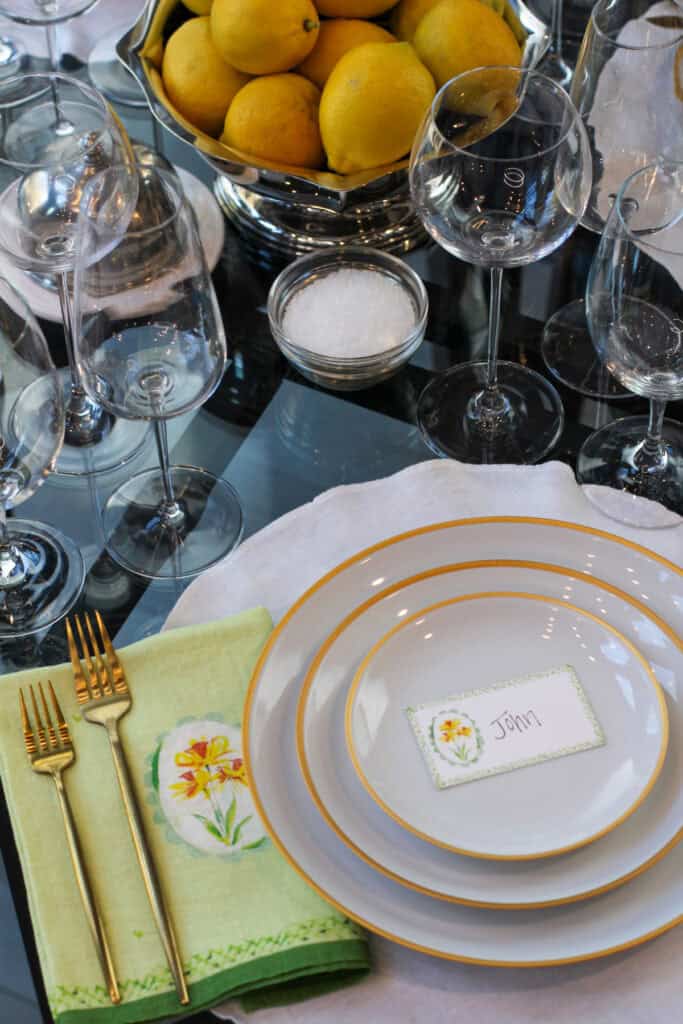 Spring table setting with green floral linens, gold utensils, personalized place cards, and lemon centerpiece
