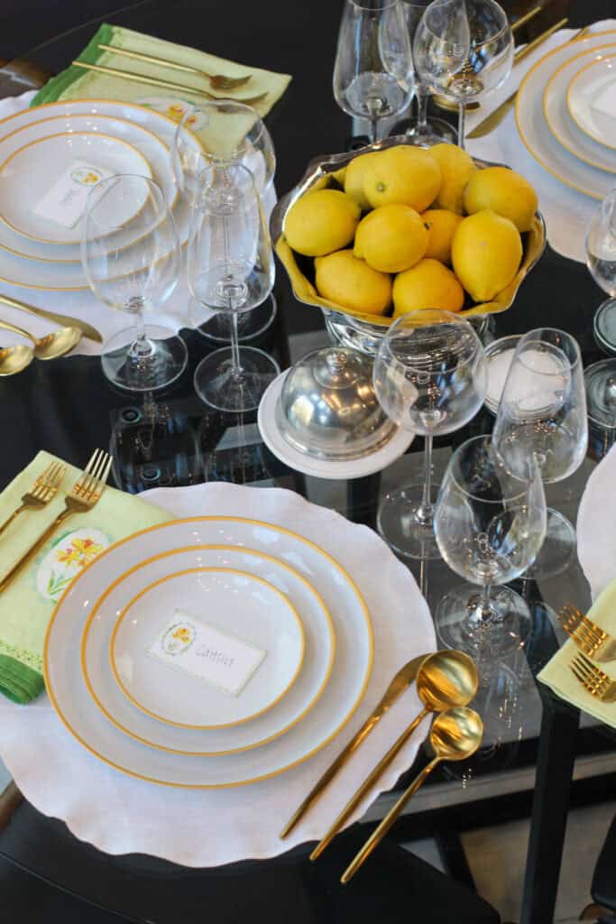 Simple elegant spring tablescape with layered plates, linen napkins, gold flatware, glassware, and lemon centerpiece