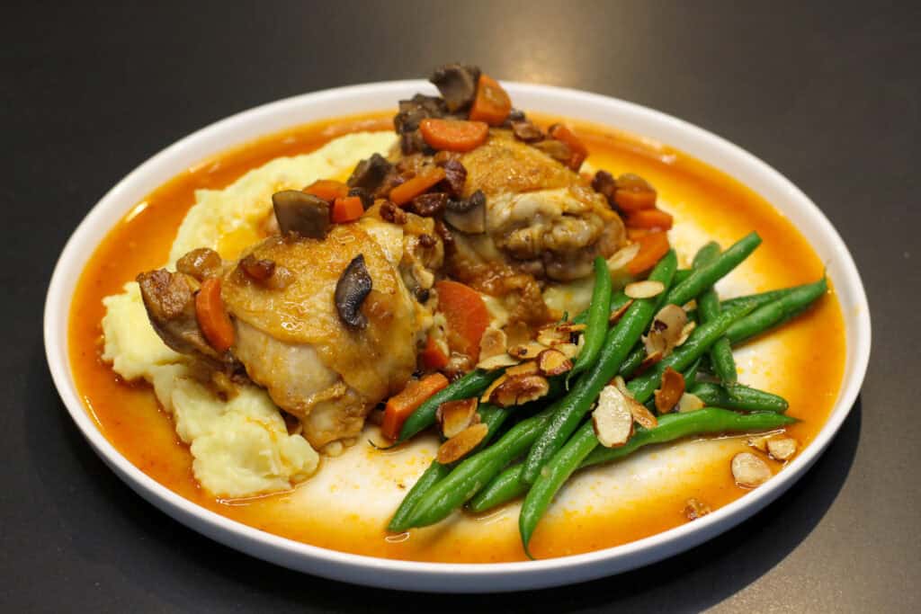 French countryside chicken with creamy mashed potatoes, sautéed mushrooms, carrots, crispy pancetta, and green beans with toasted almonds in a light pan sauce.