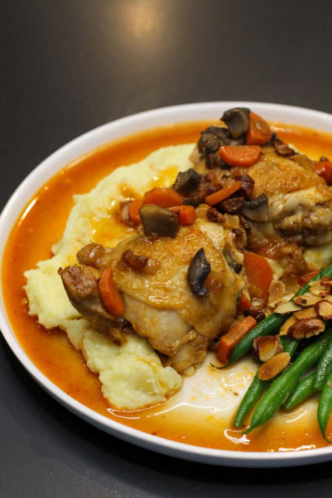French countryside chicken with creamy mashed potatoes, sautéed mushrooms, carrots, crispy pancetta, and green beans with toasted almonds in a light pan sauce.