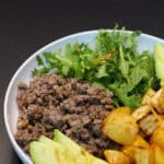 Hot honey ground venison sweet potato bowl with avocado, arugula, and roasted sweet potatoes in a white bowl