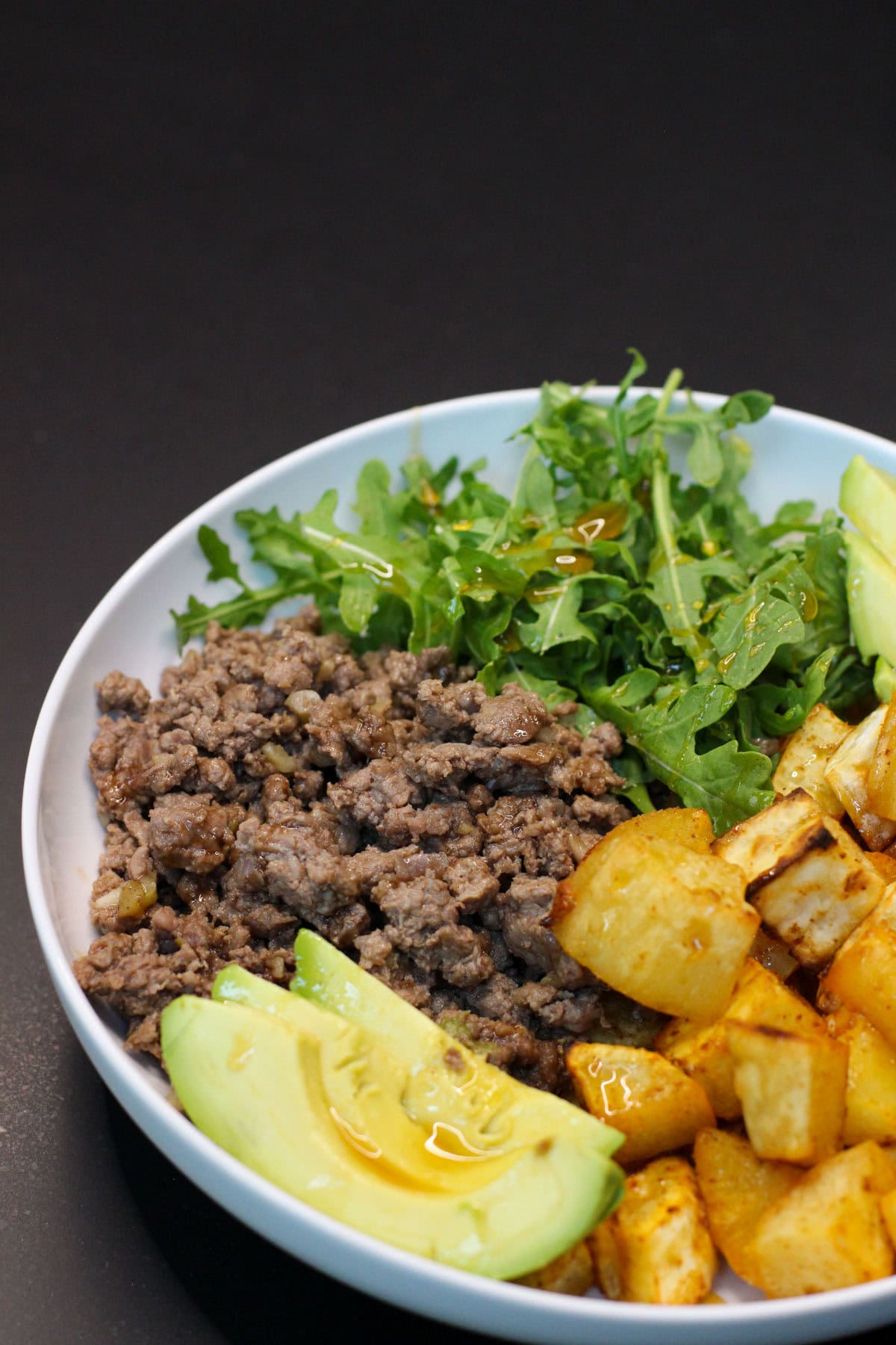 Hot honey ground venison sweet potato bowl with avocado, arugula, and roasted sweet potatoes in a white bowl