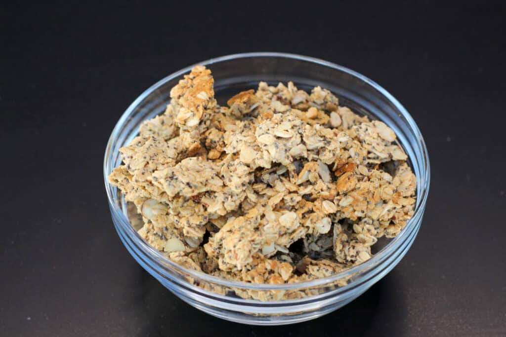 Crunchy homemade protein granola served in a glass bowl on a black background.