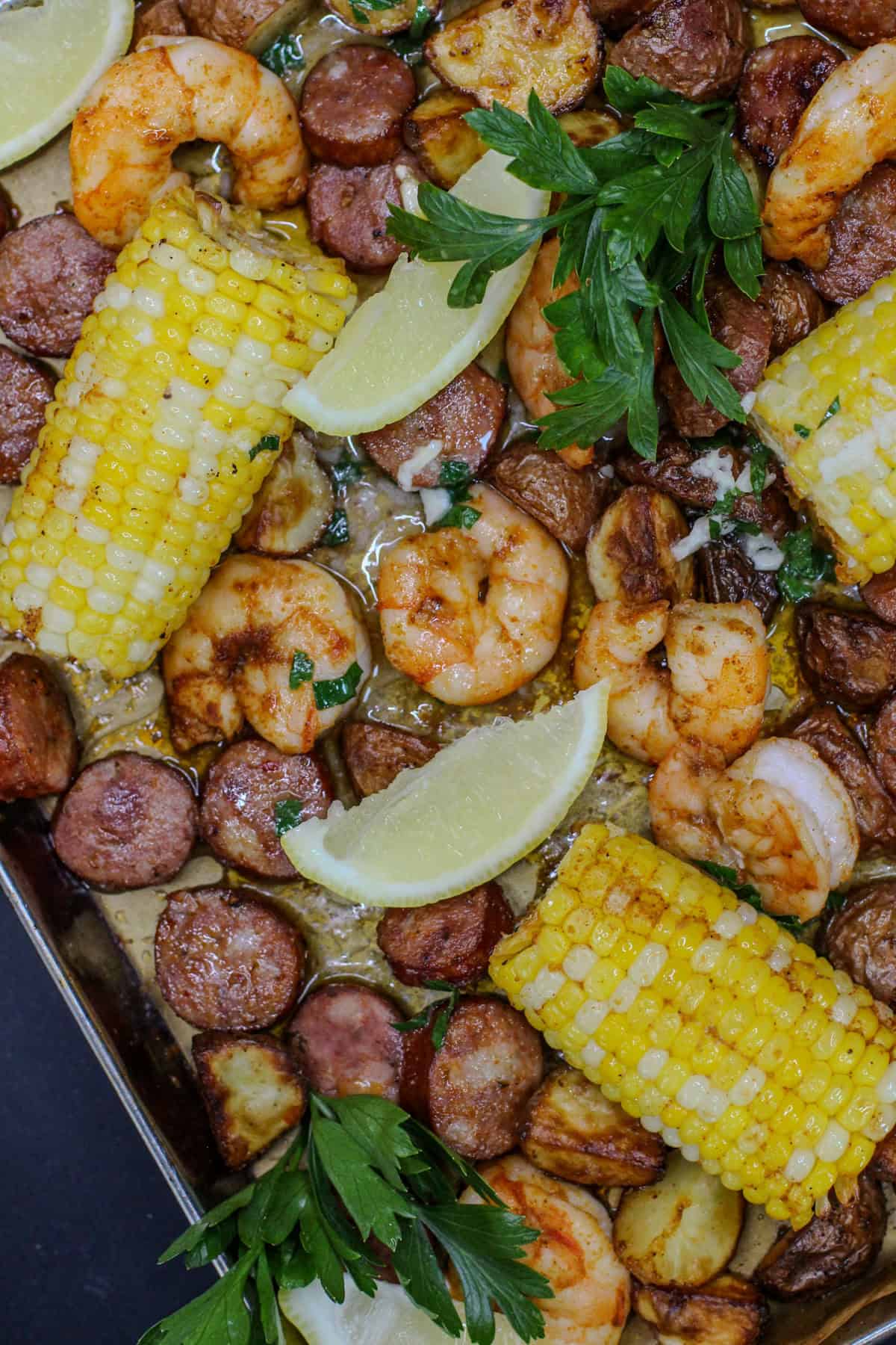 Easy sheet pan garlic butter shrimp boil with roasted baby potatoes, smoked sausage, sweet corn, fresh parsley, and lemon wedges on a baking sheet.