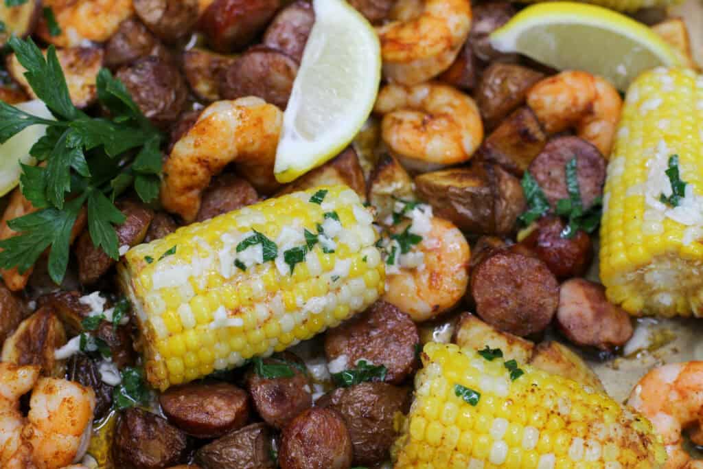 Close-up of sheet pan shrimp boil with garlic butter, roasted corn, smoked sausage, baby potatoes, fresh parsley, and juicy shrimp.