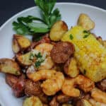 Bowl of garlic butter sheet pan shrimp boil featuring roasted shrimp, smoked sausage, crispy baby potatoes, sweet corn, and fresh herbs.