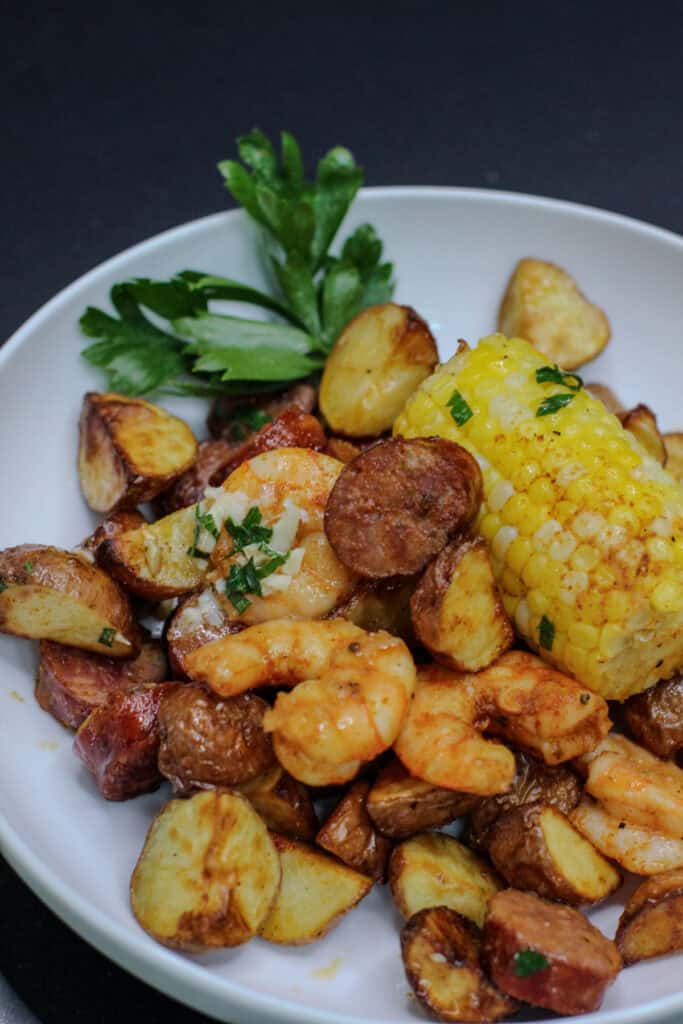Bowl of garlic butter sheet pan shrimp boil featuring roasted shrimp, smoked sausage, crispy baby potatoes, sweet corn, and fresh herbs.