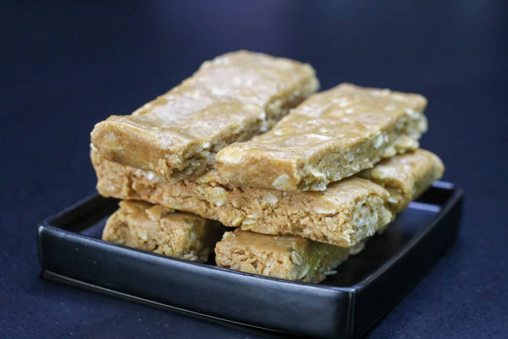 Homemade no-bake peanut butter protein bars stacked on a black serving tray, showing their soft and chewy texture with visible oats throughout.