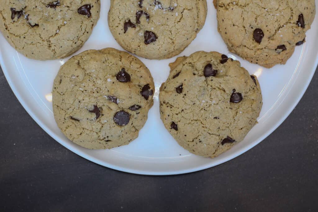 Sea salt espresso chocolate chip cookies arranged on a white serving plate, topped with chocolate chips and flaky sea salt.