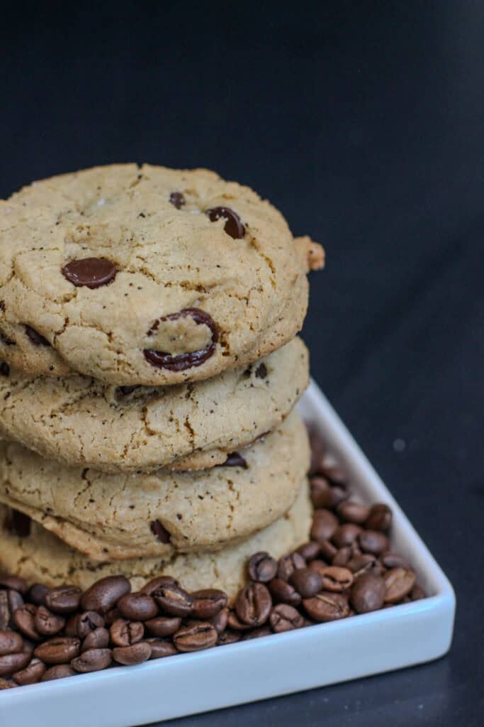 Stack of sea salt espresso chocolate chip cookies surrounded by roasted coffee beans, highlighting the espresso flavor in the cookies.