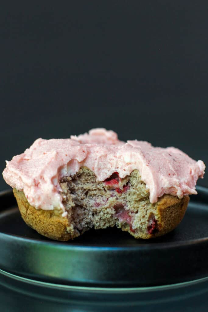 Cross-section of a baked strawberry cake donut showing fresh strawberries inside and topped with strawberry buttercream frosting.