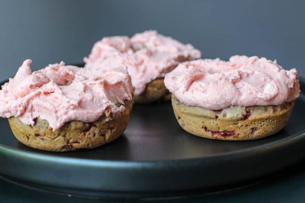 Homemade baked strawberry buttercream donuts arranged on a black serving plate.