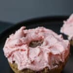 Gluten-free strawberry buttercream donut topped with fluffy homemade strawberry frosting on a black serving plate.