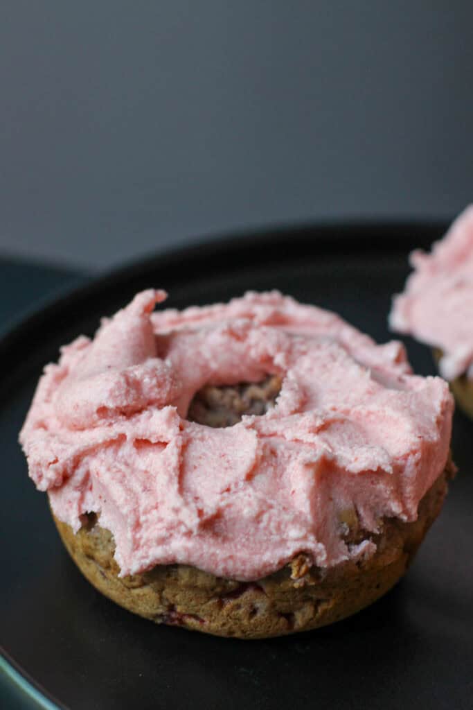 Gluten-free strawberry buttercream donut topped with fluffy homemade strawberry frosting on a black serving plate.