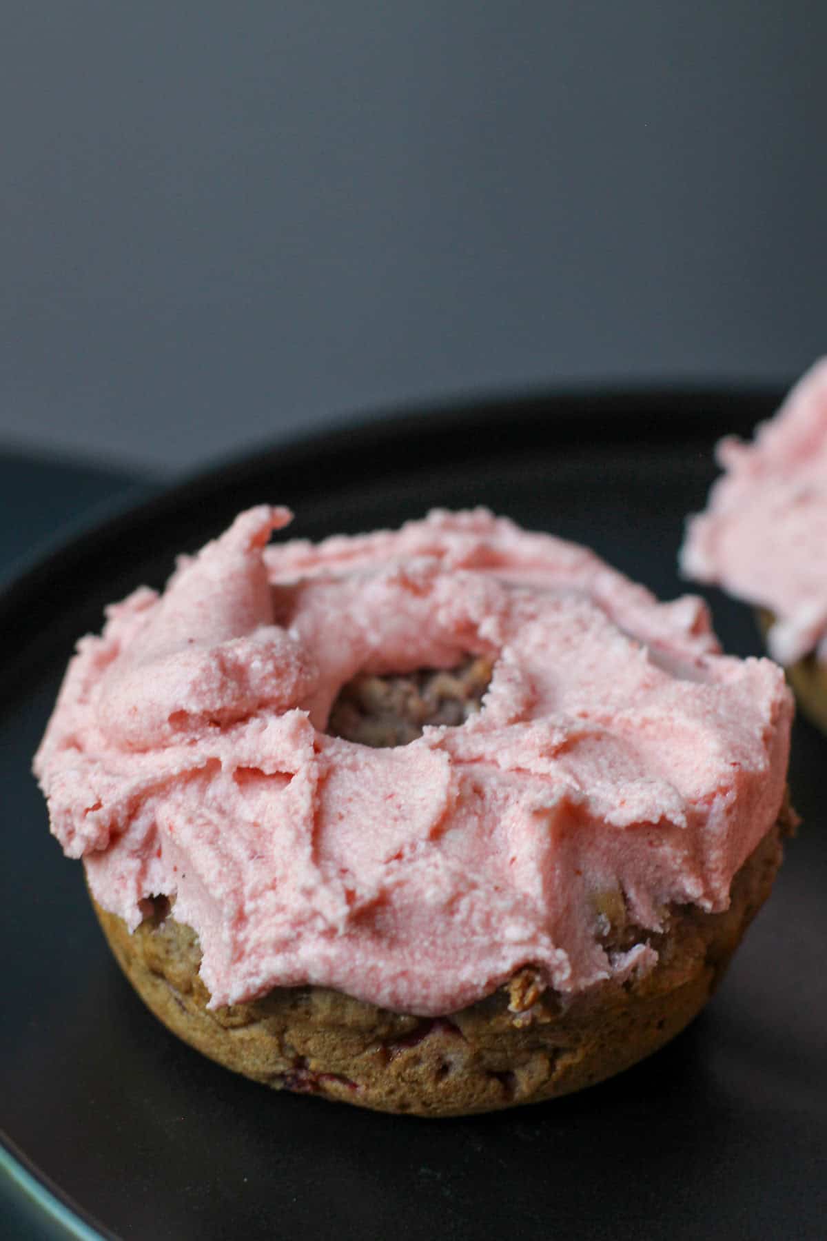 Gluten-free strawberry buttercream donut topped with fluffy homemade strawberry frosting on a black serving plate.