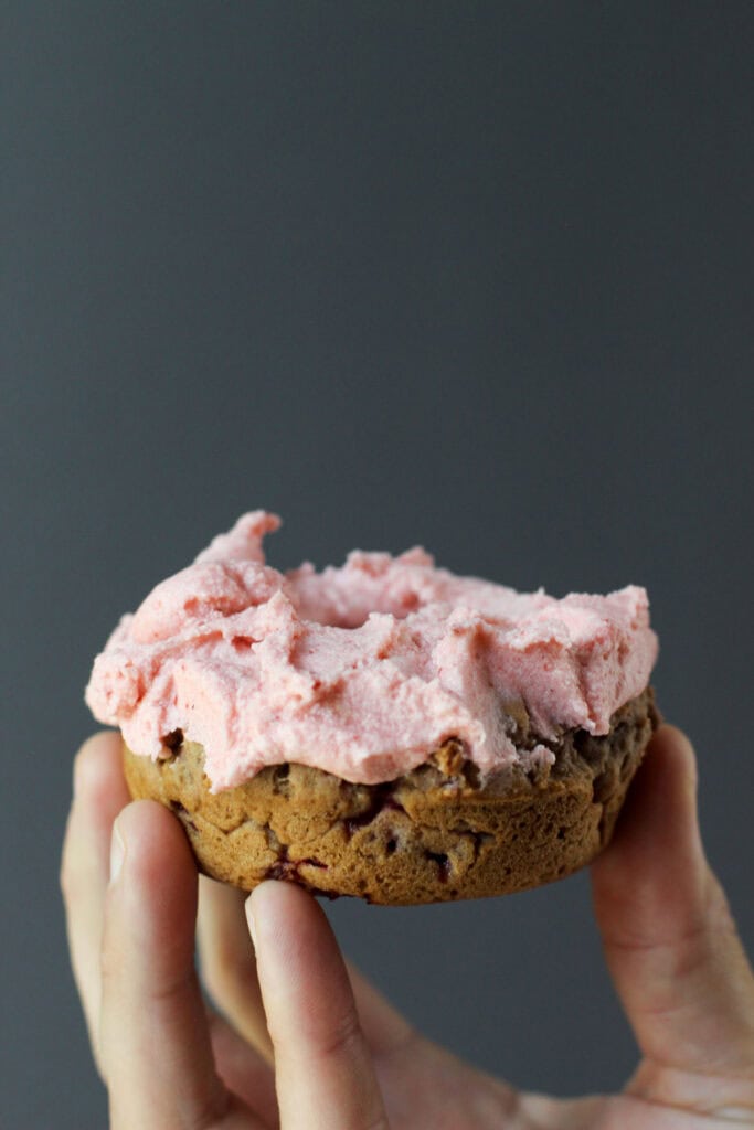 Hand holding a homemade gluten-free strawberry buttercream donut.