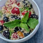 Summer Berry Quinoa Salad with fresh raspberries, blueberries, blackberries, feta cheese, pistachios, mint, and citrus honey dressing served in a white bowl.