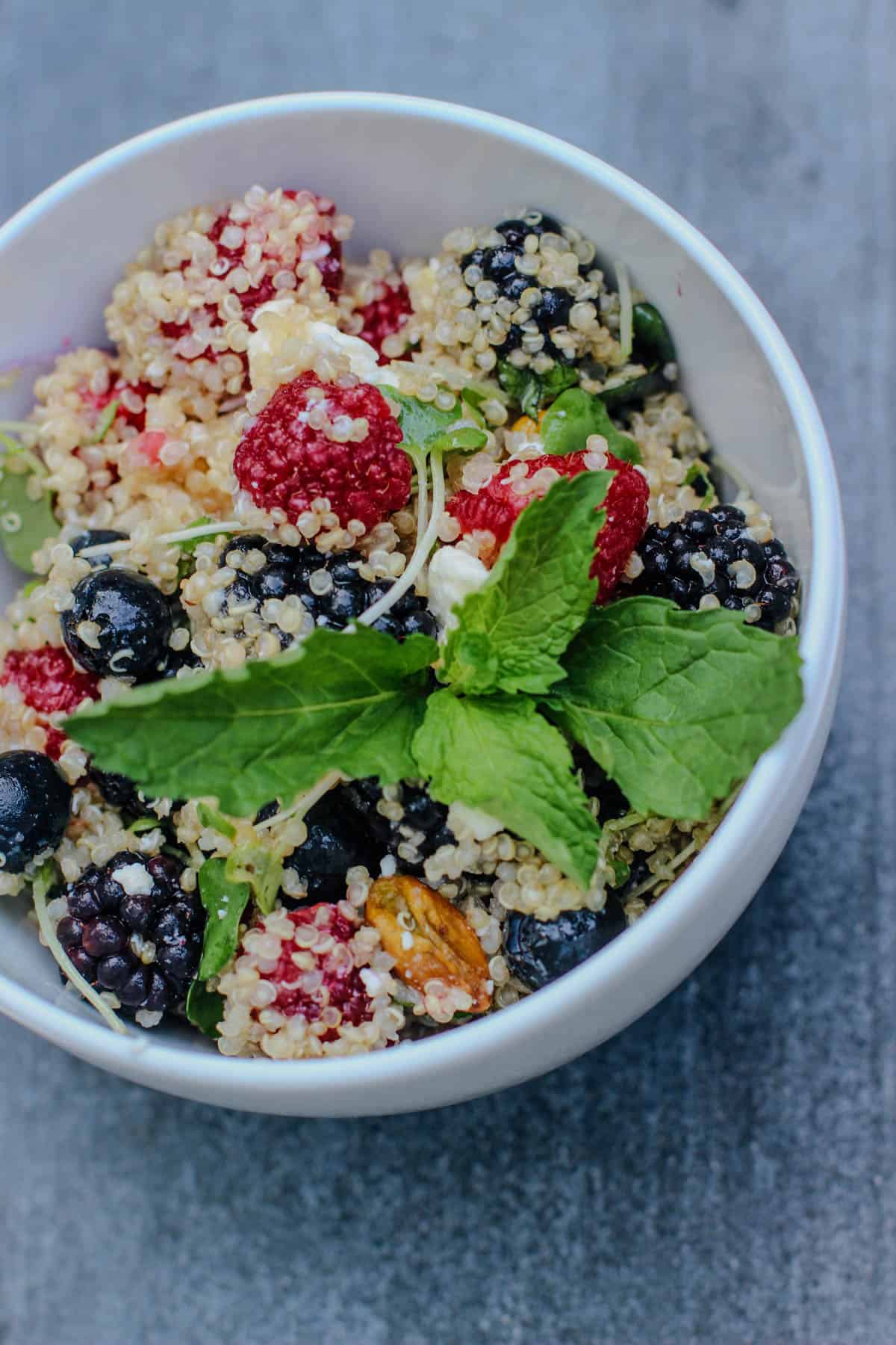 Summer Berry Quinoa Salad with fresh raspberries, blueberries, blackberries, feta cheese, pistachios, mint, and citrus honey dressing served in a white bowl.